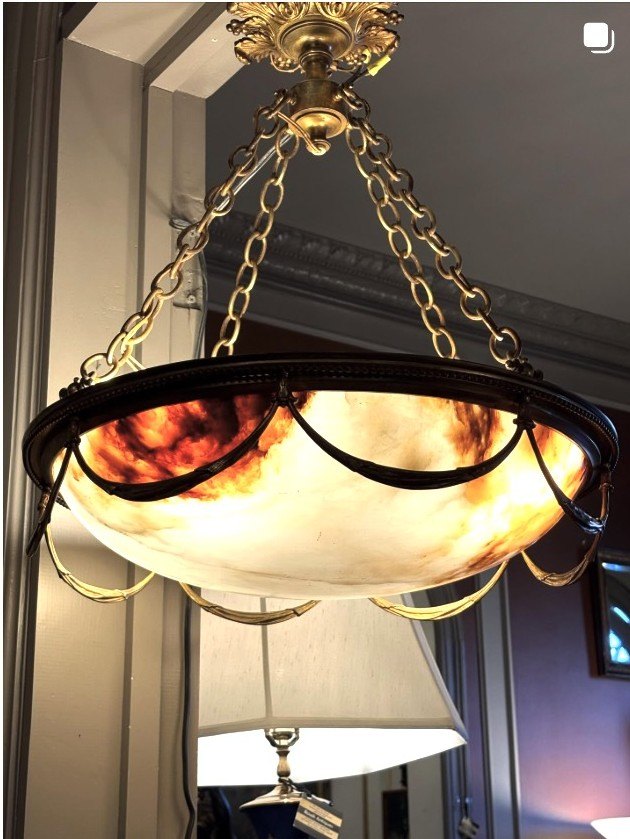 Carved alabaster dome chandelier with gilt-bronze chains, glowing warm amber when lit.