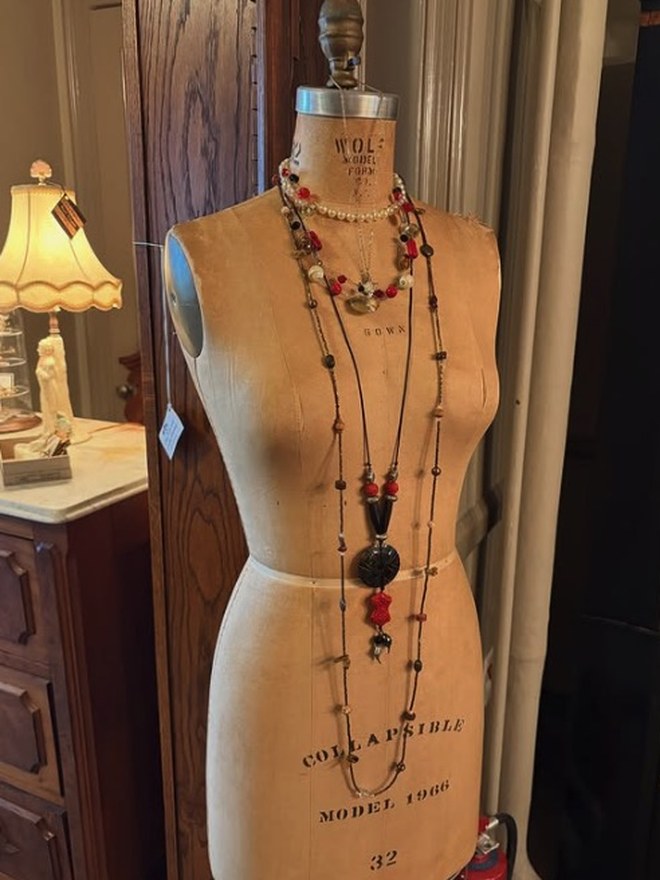 Antique tailor's dress form stamped 'Wolf Model' and 'Collapsible Model 1966, size 32,' draped with layered beaded necklaces.