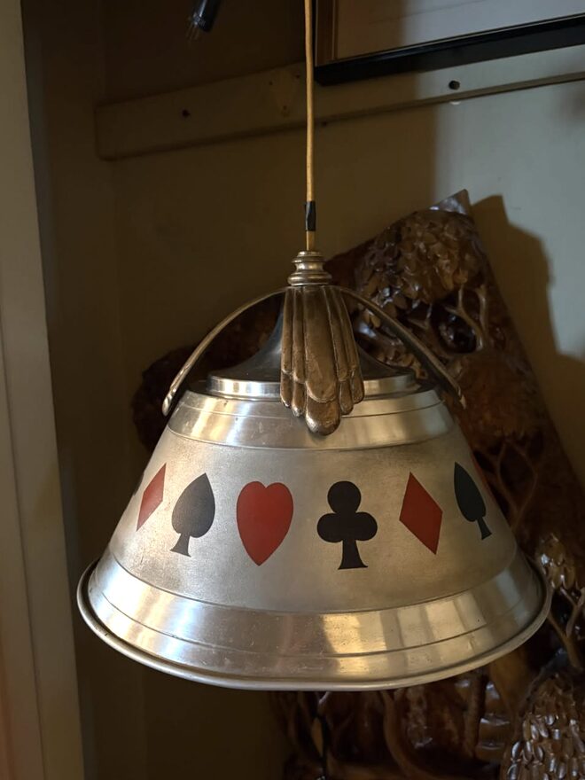 Hanging pendant light with a spun metal shade painted with a band of red and black spades, hearts, clubs, and diamonds, hung from a cast fan-shaped bracket.