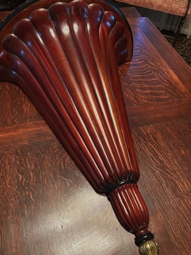 Carved mahogany wall bracket shaped like a fluted plume or shell, finished in deep red mahogany with a gilt tip.