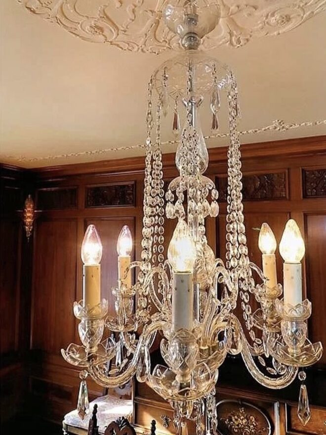Cut-glass chandelier with scrolled glass arms, candle-sleeve lights set in cut bobeches, and long swags of octagonal prisms falling from a glass crown, finished with spear drops.