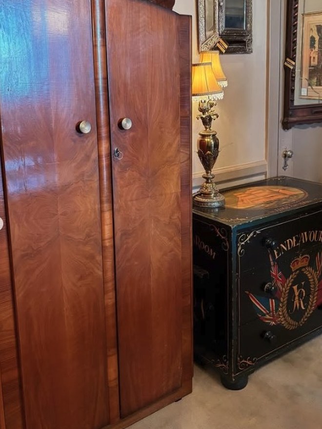 Art Deco waterfall wardrobe in figured walnut with rounded doors, beside a black painted campaign chest lettered 'Endeavour' with a Union Jack crest.