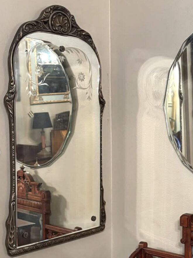 Arched wall mirror in a silvered frame cast with leaves and a scallop-shell crest, the beveled glass wheel-etched with a floral spray in the upper corner and held by rosette clips.