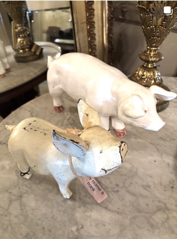 Two painted cast-iron pig figures; the front one wears a tag reading ‘my name is frank.’
