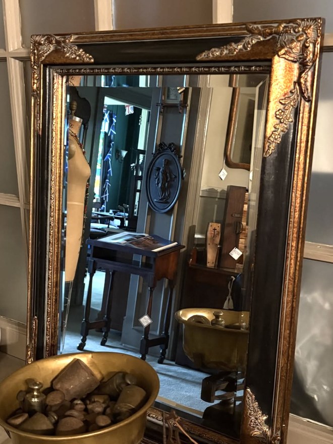 Large floor mirror with beveled glass in a black and gilt frame, ornate gilt scrollwork at each corner and an etched border running inside the glass.