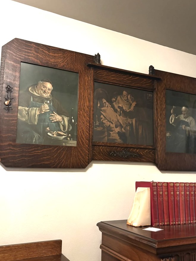 Set of three cellar-monk prints in quartersawn oak frames hung as a triptych, the center frame fitted with a small carved shelf.