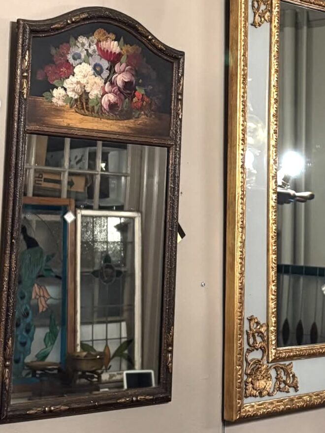 Trumeau-style wall mirror with an arched top panel painted with a basket of pink and red peonies, white blooms, and blue morning glories on a dark ground, over a mirror plate in a dark carved frame with gilt highlights.