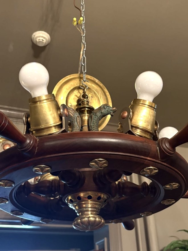 Chandelier made from a mahogany ship's wheel, with brass candle sockets standing between the spokes, brass star studs around the rim, and cast dolphin mounts at the center.